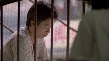 Movie still from “Dust in the Wind” (1986), directed by Hsiao-Hsien Hou – A man sitting behind bars looking down at the ground; Close Up shot, Low angle
