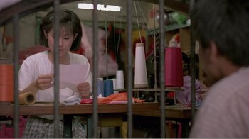 Movie still from “Dust in the Wind” (1986), directed by Hsiao-Hsien Hou – A woman sitting at a table with sewing supplies on it; Medium shot, Low angle