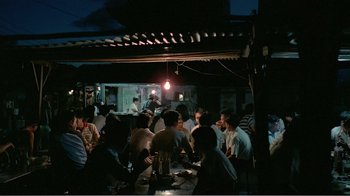 Movie still from “Dust in the Wind” (1986), directed by Hsiao-Hsien Hou – A group of people sitting at a table in front of a light; Extreme Wide shot, High angle