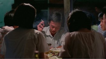 Movie still from “Dust in the Wind” (1986), directed by Hsiao-Hsien Hou – A man sitting at a dinner table smoking a cigarette; Medium shot, Over the shoulder angle