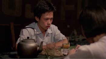 Movie still from “Dust in the Wind” (1986), directed by Hsiao-Hsien Hou – A man sitting at a table with a drink in front of him; Medium shot, Over the shoulder angle