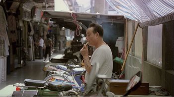 Movie still from “Dust in the Wind” (1986), directed by Hsiao-Hsien Hou – A man eating food while standing next to a motorcycle; Medium shot, High angle