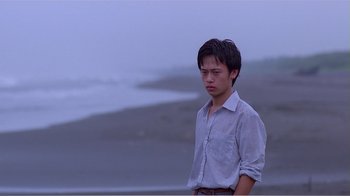 Movie still from “Dust in the Wind” (1986), directed by Hsiao-Hsien Hou – A man standing on the beach in a white shirt; Medium shot, Over the shoulder angle