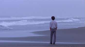 Movie still from “Dust in the Wind” (1986), directed by Hsiao-Hsien Hou – A man standing on the beach looking out at the ocean; Wide shot, Over the shoulder angle