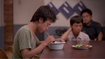 Movie still from “Dust in the Wind” (1986), directed by Hsiao-Hsien Hou – Two young men sitting at a wooden table with a bowl of food; Medium shot, Over the shoulder angle