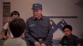 Movie still from “Dust in the Wind” (1986), directed by Hsiao-Hsien Hou – A man in a uniform talking to a group of people; Medium shot, Over the shoulder angle