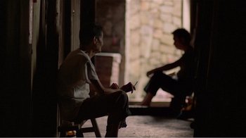 Movie still from “Dust in the Wind” (1986), directed by Hsiao-Hsien Hou – A man sitting on top of a chair next to another man; Medium shot, Over the shoulder angle