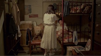 Movie still from “Dust in the Wind” (1986), directed by Hsiao-Hsien Hou – A woman standing in front of a bed in a room; Wide shot, High angle
