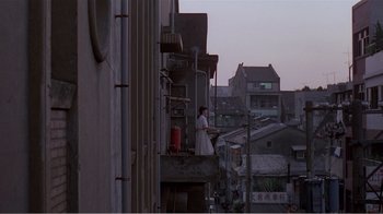 Movie still from “Dust in the Wind” (1986), directed by Hsiao-Hsien Hou – A woman standing on a balcony in the middle of a city; Extreme Wide shot, Over the shoulder angle