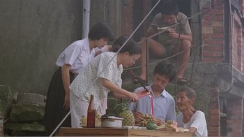 Movie still from “Dust in the Wind” (1986), directed by Hsiao-Hsien Hou – A group of people sitting around a table with a pineapple; Wide shot, High angle