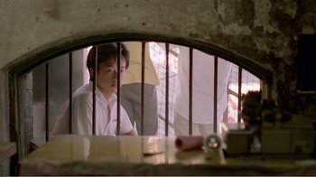 Movie still from “Dust in the Wind” (1986), directed by Hsiao-Hsien Hou – A man sitting behind bars in front of a window; Medium shot, Low angle