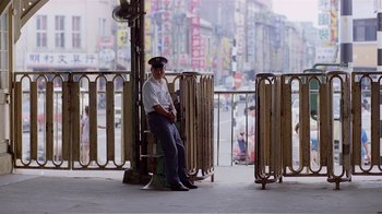 Movie still from “Dust in the Wind” (1986), directed by Hsiao-Hsien Hou – A man sitting on a bench in front of a fence; Wide shot, High angle