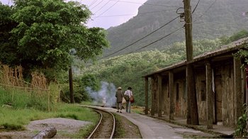 Movie still from “Dust in the Wind” (1986), directed by Hsiao-Hsien Hou – Two people walking down a train track next to a train station; Extreme Wide shot, High angle