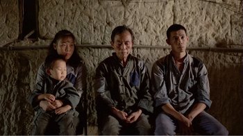 Movie still from “Dust in the Wind” (1986), directed by Hsiao-Hsien Hou – An older man and two younger men sitting next to each other with a baby; Medium shot, High angle
