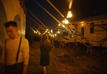 Movie still from “EO” (2022), directed by Jerzy Skolimowski – A woman is standing in a field with lights hanging above her head; Wide shot, Over the shoulder angle