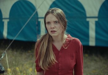 Movie still from “EO” (2022), directed by Jerzy Skolimowski – A woman in a red shirt standing in front of a tent; Medium shot, Over the shoulder angle