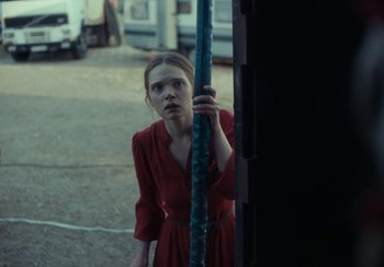 Movie still from “EO” (2022), directed by Jerzy Skolimowski – A woman in a red dress is leaning against a pole; Medium shot, Over the shoulder angle