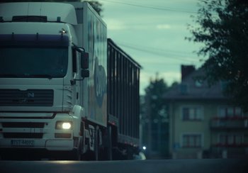 Movie still from “EO” (2022), directed by Jerzy Skolimowski – A truck driving down a street next to a building; Extreme Wide shot, Low angle