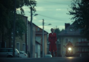 Movie still from “EO” (2022), directed by Jerzy Skolimowski – A woman in a red dress standing on the side of the road; Extreme Wide shot, Low angle