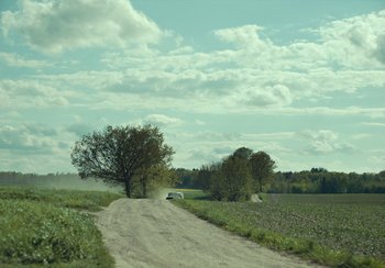 Movie still from “EO” (2022), directed by Jerzy Skolimowski – A car driving down a dirt road near a field; Extreme Wide shot, High angle