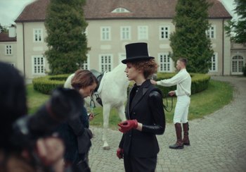 Movie still from “EO” (2022), directed by Jerzy Skolimowski – A woman in a top hat stands next to a white horse; Medium shot, Over the shoulder angle