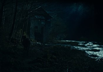 Movie still from “EO” (2022), directed by Jerzy Skolimowski – A person standing in front of a building in the dark; Extreme Wide shot, High angle