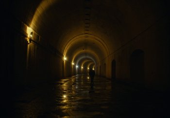 Movie still from “EO” (2022), directed by Jerzy Skolimowski – A person is standing in a dark tunnel with lights on; Extreme Wide shot, High angle