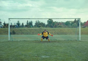 Movie still from “EO” (2022), directed by Jerzy Skolimowski – A man standing on a field holding a frisbee; Wide shot, Low angle