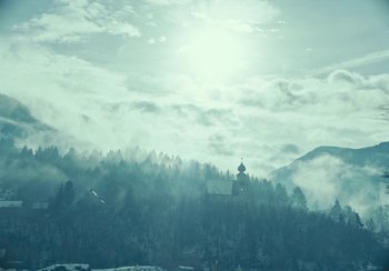 Movie still from “EO” (2022), directed by Jerzy Skolimowski – The sun is shining over a mountain with a church in the distance; Extreme Wide shot, Low angle