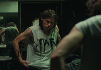 Movie still from “EO” (2022), directed by Jerzy Skolimowski – A man in a white t - shirt is looking at himself in the mirror; Medium shot, Over the shoulder angle