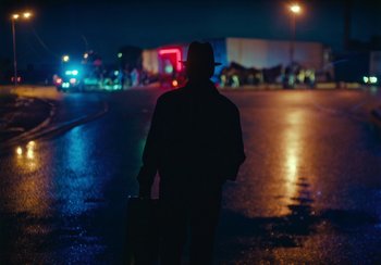 Movie still from “EO” (2022), directed by Jerzy Skolimowski – A man in a hat and jacket walking down a street; Wide shot, Low angle