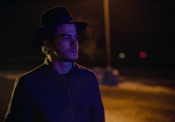 Movie still from “EO” (2022), directed by Jerzy Skolimowski – A man wearing a black hat standing in the dark; Close Up shot, Over the shoulder angle