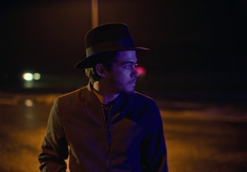 Movie still from “EO” (2022), directed by Jerzy Skolimowski – A young man wearing a black hat standing in the dark at night; Close Up shot, Low angle