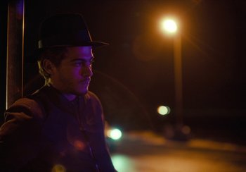 Movie still from “EO” (2022), directed by Jerzy Skolimowski – A man wearing a hat standing in front of a street light; Close Up shot, Over the shoulder angle
