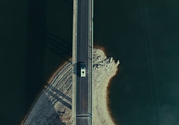 Movie still from “EO” (2022), directed by Jerzy Skolimowski – An aerial view of a car driving on a bridge over a river; Extreme Wide shot, Overhead angle