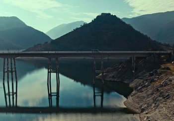 Movie still from “EO” (2022), directed by Jerzy Skolimowski – A bridge over a body of water with mountains in the background; Extreme Wide shot, High angle