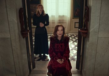 Movie still from “EO” (2022), directed by Jerzy Skolimowski – Two women are standing in a doorway and one of them is sitting on a chair; Medium shot, High angle