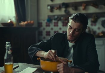 Movie still from “EO” (2022), directed by Jerzy Skolimowski – A man sitting at a table in front of a bowl of food; Medium shot, Low angle