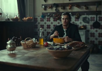 Movie still from “EO” (2022), directed by Jerzy Skolimowski – A man sitting at a wooden table with a bowl of food; Medium shot, Low angle