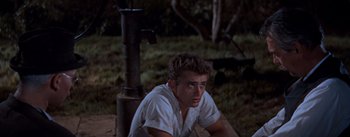 Movie still from “East of Eden” (1955), directed by Elia Kazan – A man sitting on the ground in front of a water pump; Medium shot, High angle