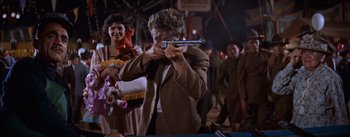 Movie still from “East of Eden” (1955), directed by Elia Kazan – A man holding a gun while standing in front of a crowd of onlookers; Medium shot, Over the shoulder angle