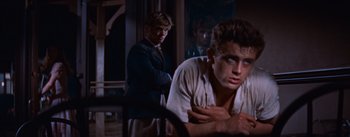 Movie still from “East of Eden” (1955), directed by Elia Kazan – Two young men in a dark room , one of them leaning on the wall; Medium shot, Over the shoulder angle