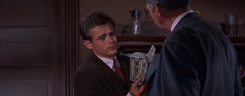 Movie still from “East of Eden” (1955), directed by Elia Kazan – A man in a suit and tie holding a stack of money; Close Up shot, Over the shoulder angle