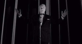 Movie still from “Ed Wood” (1994), directed by Tim Burton – A man in a suit and tie holding a microphone in front of a curtain; Medium shot, Low angle