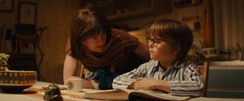 Movie still from “Eddie the Eagle” (2015), directed by Dexter Fletcher – A woman and a boy are sitting at a table reading books; Medium shot, Over the shoulder angle