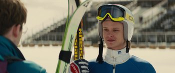 Movie still from “Eddie the Eagle” (2015), directed by Dexter Fletcher – A man holding a pair of skis in his hands; Close Up shot, Over the shoulder angle