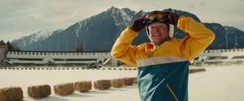 Movie still from “Eddie the Eagle” (2015), directed by Dexter Fletcher – An older man in a yellow and blue ski jacket; Medium shot, Low angle