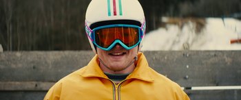 Movie still from “Eddie the Eagle” (2015), directed by Dexter Fletcher – A man in a yellow jacket wearing a helmet and goggles; Close Up shot, Low angle