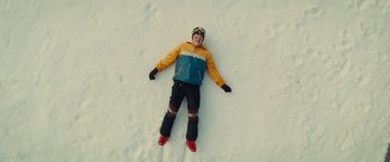 Movie still from “Eddie the Eagle” (2015), directed by Dexter Fletcher – A man laying in the snow wearing a helmet; Wide shot, Overhead angle