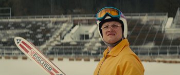 Movie still from “Eddie the Eagle” (2015), directed by Dexter Fletcher – A man wearing a yellow jacket and a helmet; Close Up shot, Low angle